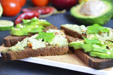 Guacamole with bread and avocado Sandwich with avocado and guacamole. Black cereal bread. Ingredients for making lime, red pepper, tomatoes. Healthy food, diet on a black background