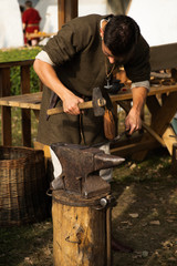Reconstruction of old crafts. A craftsman in historical clothing is hammering on the anvil. A blacksmith forges a metal product. Dressed in an old outfit.