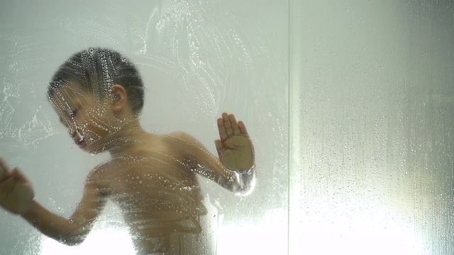 Asian boy about 3 year and 8 months playing with soap and water from shower head on bathroom glass