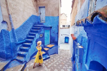 Photo sur Plexiglas Maroc Voyage coloré par le Maroc. Jeune femme en robe jaune marchant dans la médina de la ville bleue de Chefchaouen.