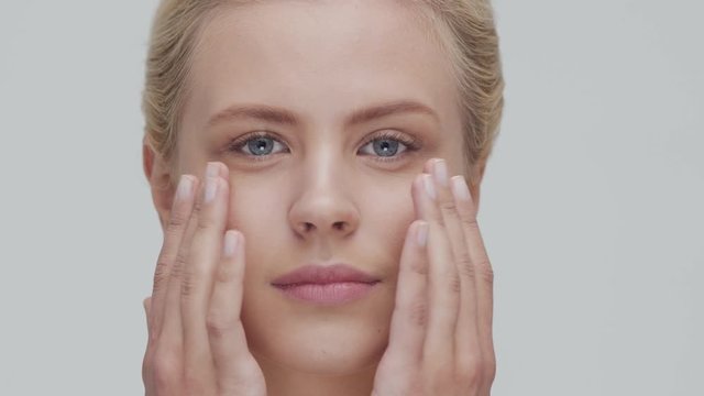 Studio portrait of young, beautiful and natural blond woman applying skin care cream. Face lifting, cosmetics and make-up.