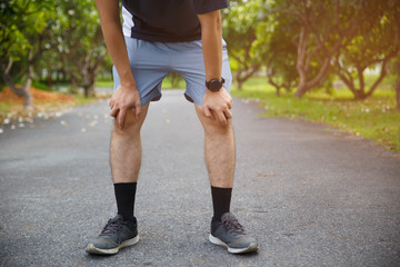 Male runner athlete knee injury and pain. Man suffering from painful knee while running in the public park.