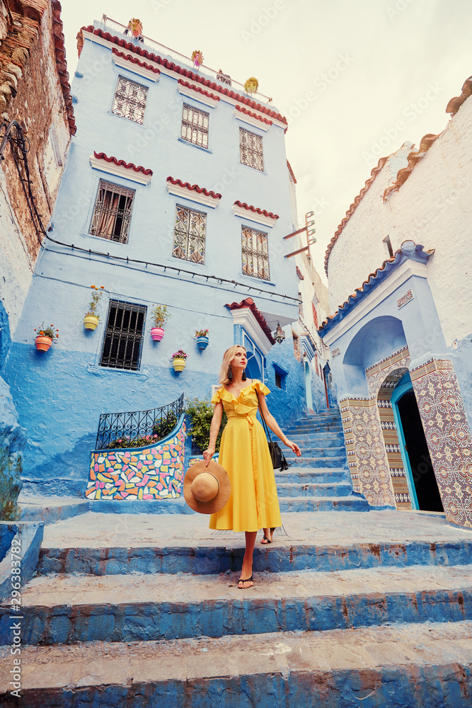 Wall mural Colorful traveling by Morocco. Young woman in yellow dress walking in  medina of  blue city Chefchaouen.