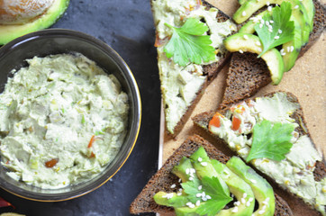 Guacamole with bread and avocado Sandwich with avocado and guacamole. Black cereal bread. Ingredients for making lime, red pepper, tomatoes. Healthy food, diet on a black background