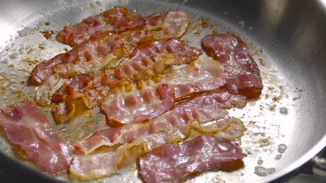 Bacon strips sizzling on a frying steel pan