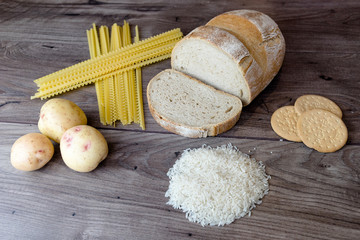 Common bad carbohydrates to avoid such as white bread, pasta, rice, potatoes and buscuits laying on top of a wooden table viewed from above