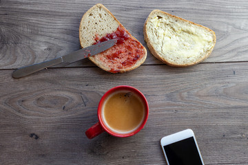 A white bread slice with spread jam on it viewed from above and a red coffee mug on a wooden table