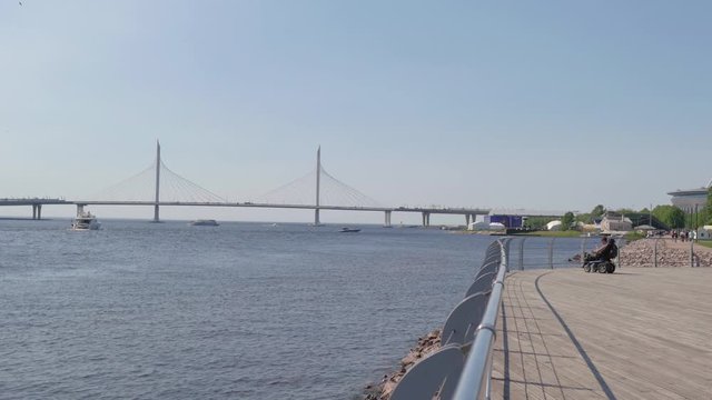 A man in a wheelchair on the promenade on the background of the bridge. A disabled person walks by the river alone