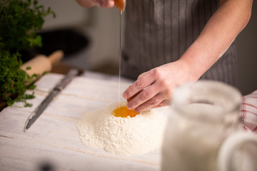 Obraz na płótnie Canvas A woman sticks an egg into flour, prepares homemade pasta dough