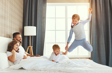 happy family mother, father and children laughing, playing and jumping in bed   at home.