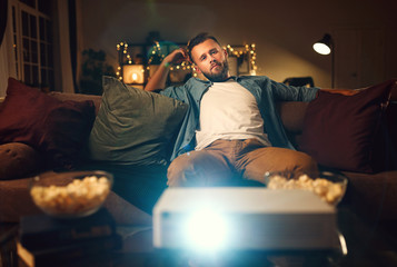 young man watching projector tv at home in   evening alone