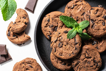 Fresh homemade chocolate cookies with green aromatic mint leaves on white background with copy space for your text. Template food blog social media. 