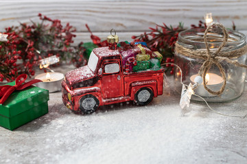 Festive Christmas composition with red toy car, gift boxes, candles and decor on white wooden background.