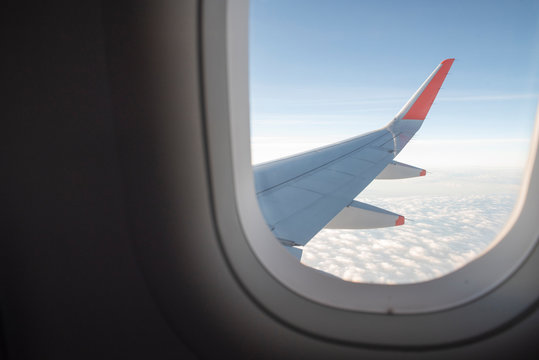 View From Inside Airplane Window. Looking Outside At The Airplane Wing Seeing Clouds And A Blue Sky.