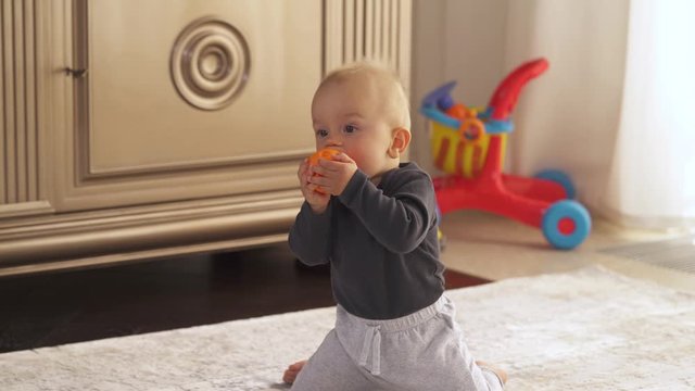 Adorable toddler boy holding and chewing small orange ball. Joyful kid playing with a toy. Happy childhood concept