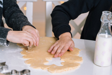Detail of young kids baking Christmas gingerbread cookies in house kitchen on winter day. child's hands preparing cookies using cookie cuttersю Cooking with children for XMas at home. Selective focus
