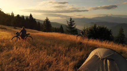 4k drone clip with two mountain bikes and a tent on a mountain meadow at sunrise in autumn season. Adventure cycling concept. - Powered by Adobe