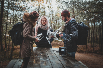 Three students are fixing broken drone using table at autumn forestal park.