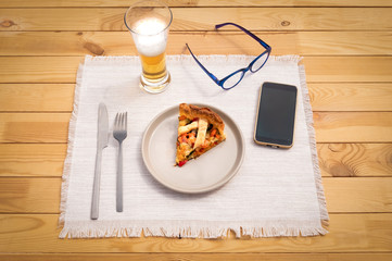 Ready for a light meal. Presentation of a slice of healthy vegan pie made of vegetables and baked. Wellness and diet. Glass of beer, eyeglasses and cellphone on the wooden table.