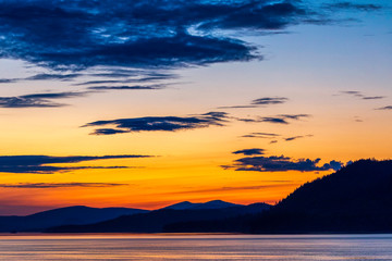 Fototapeta na wymiar Orange Setting Sunset, Mountains silhouetted, Ocean