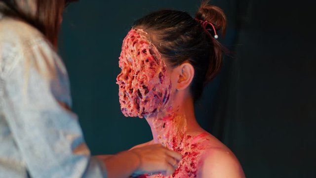 Make-up artist painting actor girl for horror film.Close up