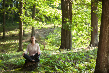 Beautiful woman meditating in the forest on a sunny morning