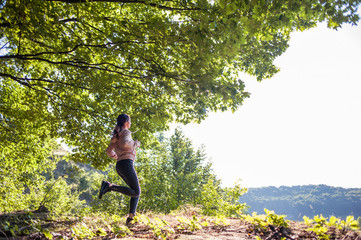 Young girl jogging in the woods on a sunny morning.