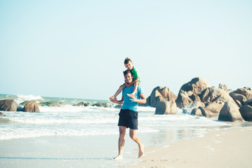 happy family on beach playing, father with son walking sea coast, rocks behind smiling taking vacation