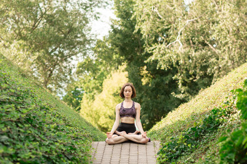 Young woman alone doing yoga on a park alley on a sunny summer day. Yoga concept
