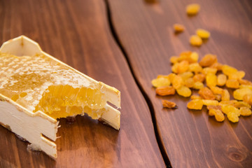 honey in honeycomb next to raisins on a wooden background