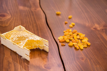 honey in honeycomb next to raisins on a wooden background