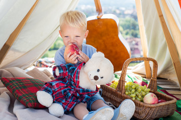 Cute little boy eating apple outdoor. Child playing with toy in summer. Has happy on camping. Little child have fun on fresh air.