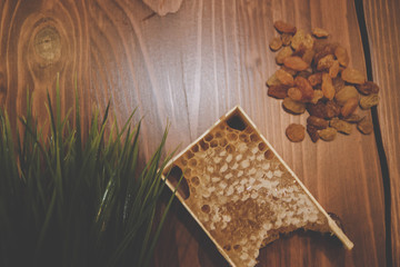honey in combs next to raisins with green grass leaves on a wooden background