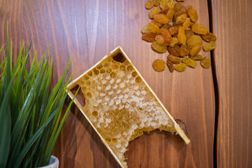 honey in combs next to raisins with green grass leaves on a wooden background