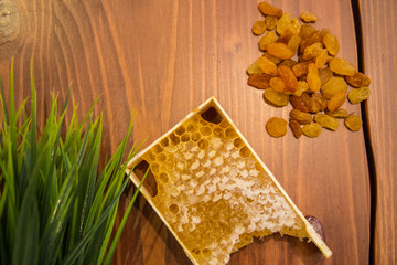 honey in combs next to raisins with green grass leaves on a wooden background