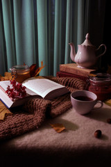 Autumn still life with an open book, with yellow leaves and a knitted scarf and tea set. Cozy still life.