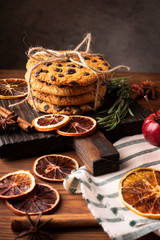 Shortbread cookies with chocolate chips on the kitchen board and dry sliced orange on a wooden background.