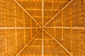 Close - up of the interior of the thatched roof with a crossbar. Use for backgrounds or textures with copy space. Thatched roof inside in the form of cobwebs . Sunny weather under the roof. Real straw