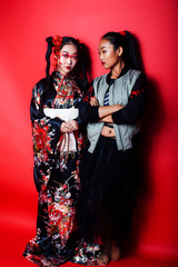 two pretty geisha girls friends: modern asian woman and traditional wearing kimono posing cheerful on red background