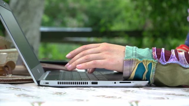 Female hands typing on the keyboard of a laptop that stands on a street table