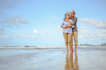 Senior couples embrace on the beach at sunny day, plan life insurance with the concept of happy retirement.