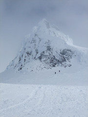 Fototapeta na wymiar Two climber make their way up past Carter Rock, an old lave dome, on Mt. Hood as clouds close in.