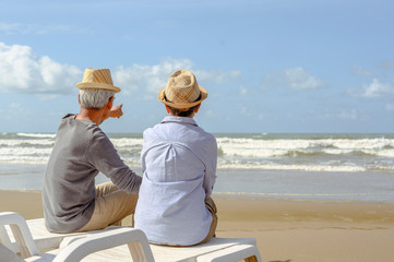 Senior couple sitting on chairs at the beach looking at the ocean on a good day and talking, plan life insurance at retirement concept.