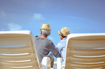 Senior couple sitting on chairs at the beach looking at the ocean on a good day and talking for to plan life insurance at retirement concept.