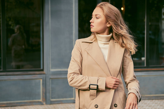 Side view of attractive girl in trench coat confidently looking away on street