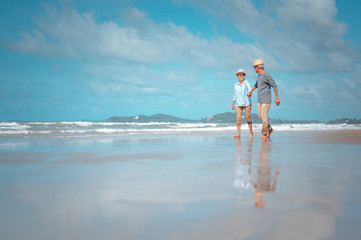 Senior couples walking hand in hand on the beach at sunny day, plan life insurance with the concept...