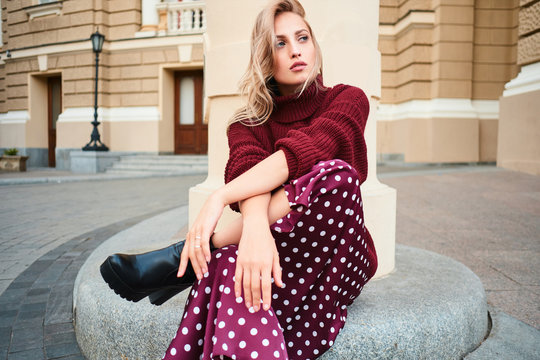 Gorgeous stylish blond girl in knitted sweater sensually looking away while posing outdoor