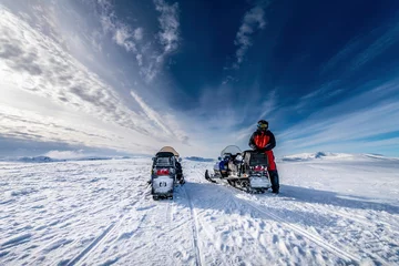 Fotobehang Two blue snowmobiles (back side) with a boy dressed for winter driving in cold mountains, he waits for his friend to continue the holiday adventure. Hemavan -Tarnaby area in Lappland, Sweden © Alexandre Patchine