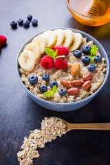 Healthy breakfast. Oatmeal with fruits, nuts and honey. Oatmeal with blueberries, banana and raspberry. Cooked oatmeal on dark background. Vegetarian food
