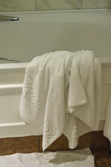 Discarded large white towel thrown over bathtub in hotel/home
